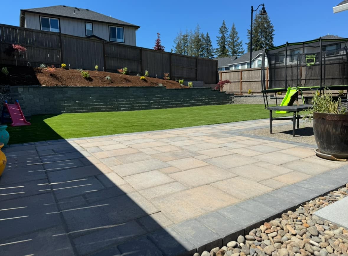 Paver patio, artificial turf lawn, and stone retaining wall combo project by GI Landscape