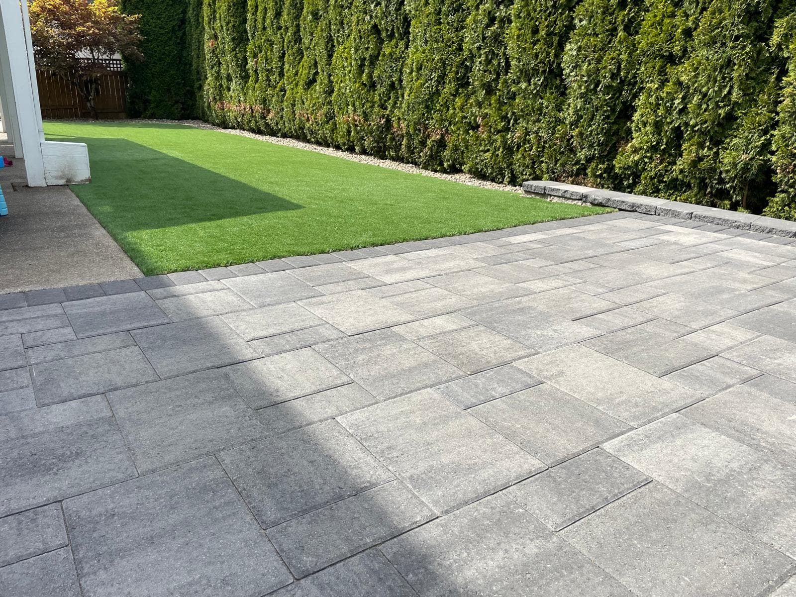Large paver patio beside an artificial-turf lawn screened by arborvitae, installed by GI Landscape