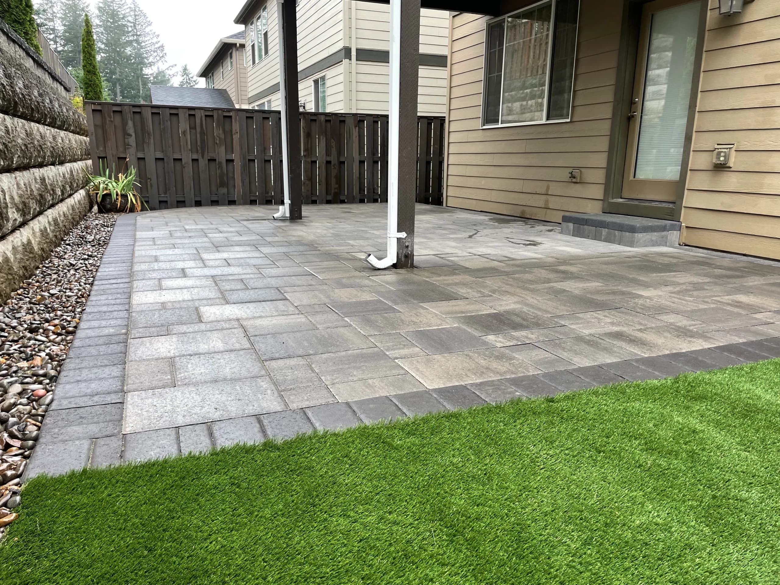 Premium paver patio with artificial turf and stone retaining wall — a full GI Landscape backyard install